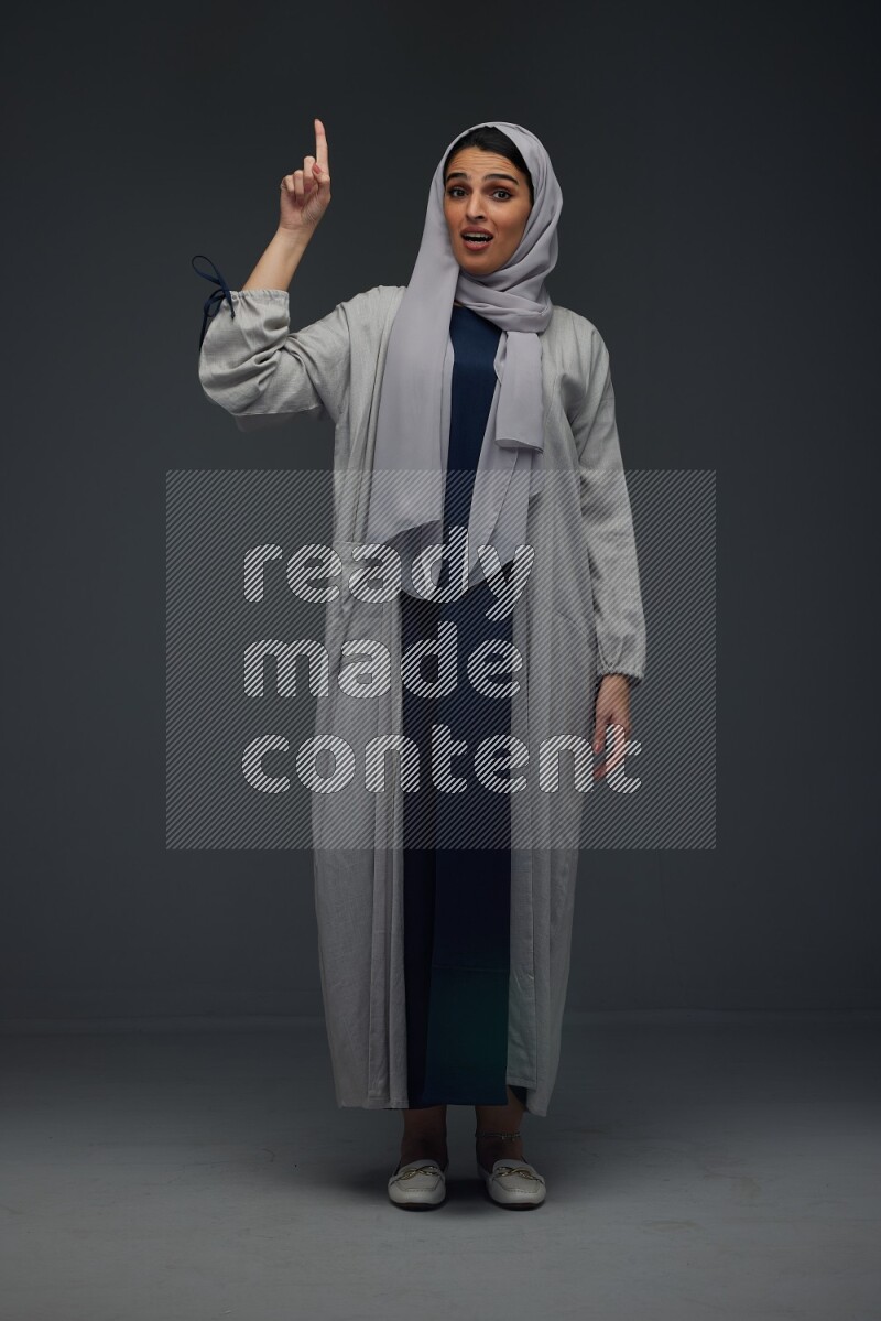 A Saudi woman wearing a light gray Abaya and head scarf standing and making multi poses eye level on a grey background