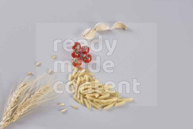 Mini penne with garlic, cherry tomatoes and wheat stalks on light grey background