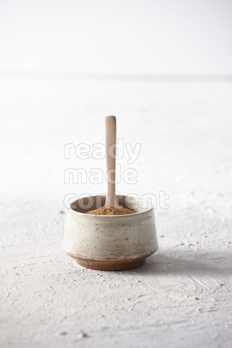 Ceramic beige bowl full of cinnamon powder with a wooden spoon on a textured white background