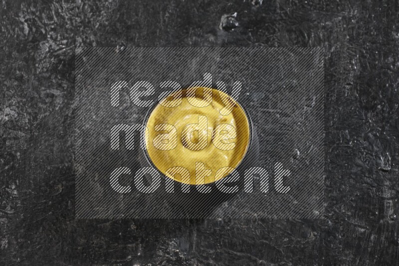 A black pottery bowl full of mustard paste on textured black flooring