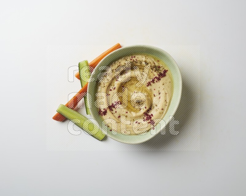 Hummus in a green plate garnished with zattar & sumak on a white background