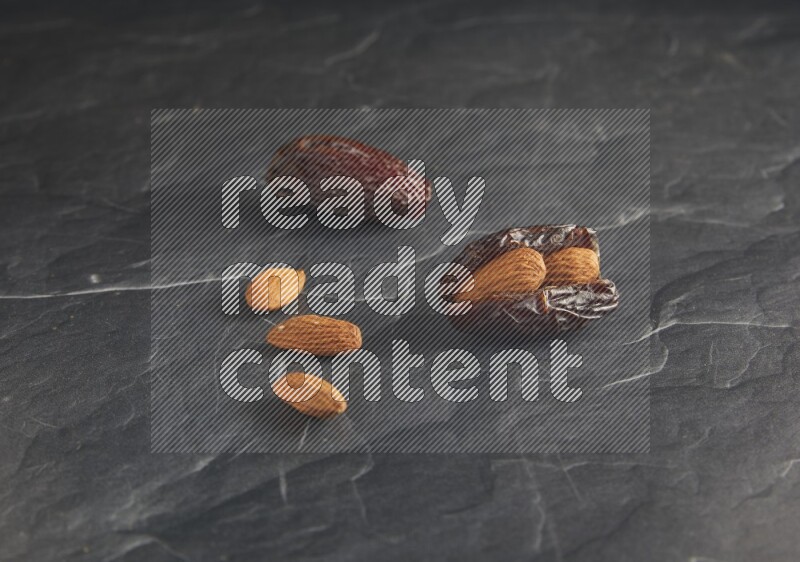 two almond stuffed madjoul dates on a black textured background