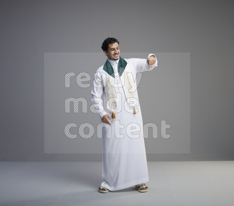 رجل سعودي يرتدي ثوب ابيض يضع شال مكتوب عليه المملكة العربية السعودية حول رقبته