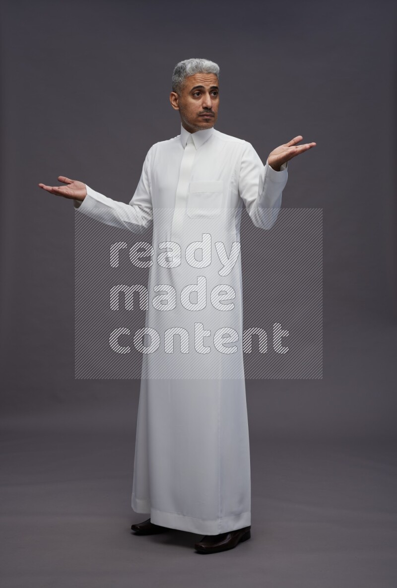 Saudi man wearing thob standing interacting with the camera on gray background