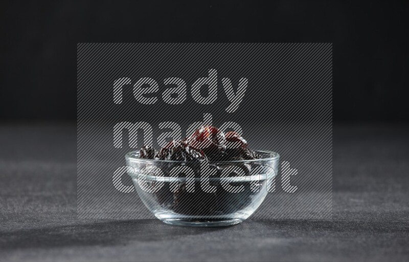A glass bowl full of dried plums on a black background in different angles