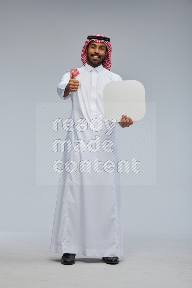 Saudi man Wearing Thob and shomag standing holding social media sign on Gray background