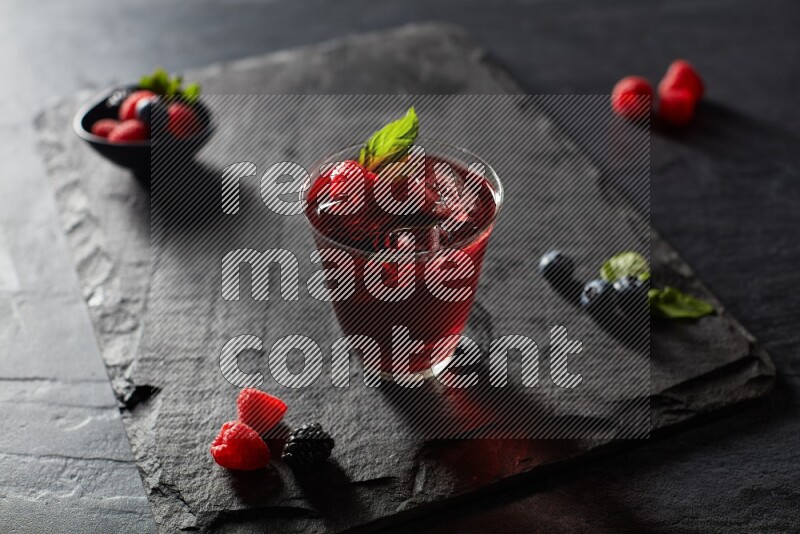 A glass of mixed berries juice with mint leaves on black background
