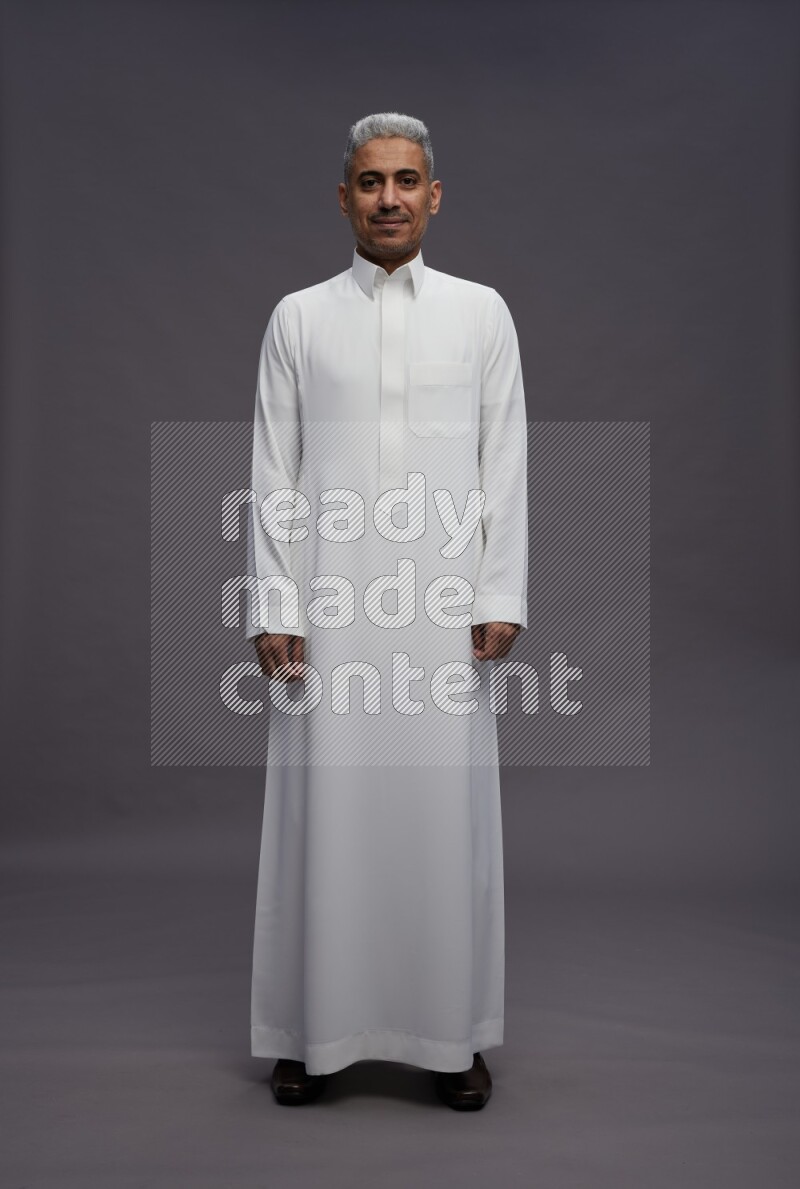 Saudi man wearing thob standing interacting with the camera on gray background