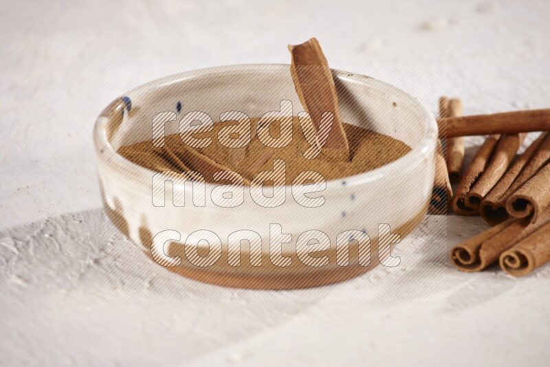 Ceramic bowl full of cinnamon powder with cinnamon sticks on the side on white background