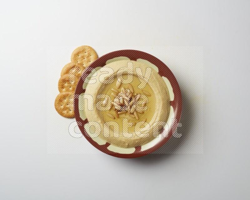 Hummus in a traditional plate garnished with pine nuts on a white background