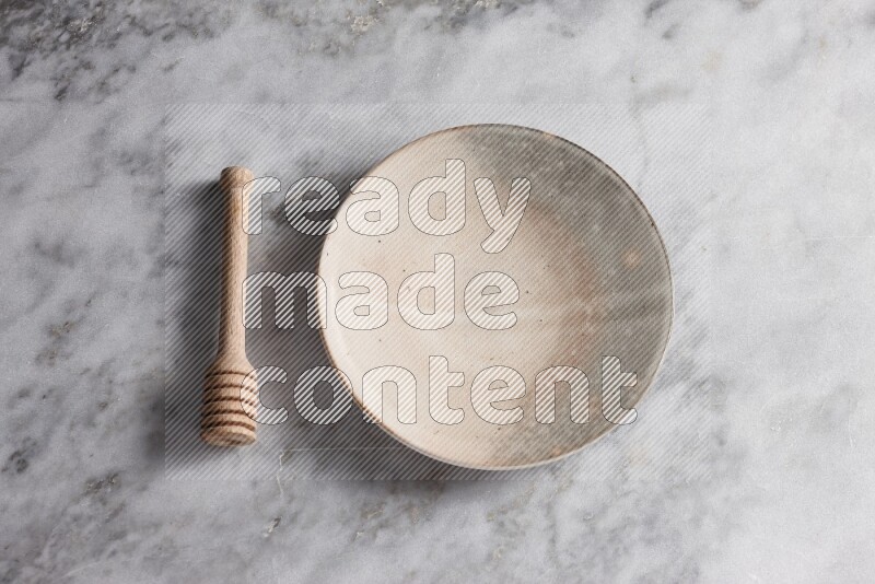 Multicolored pottery plate with wooden honey dipper on the side on grey marble background