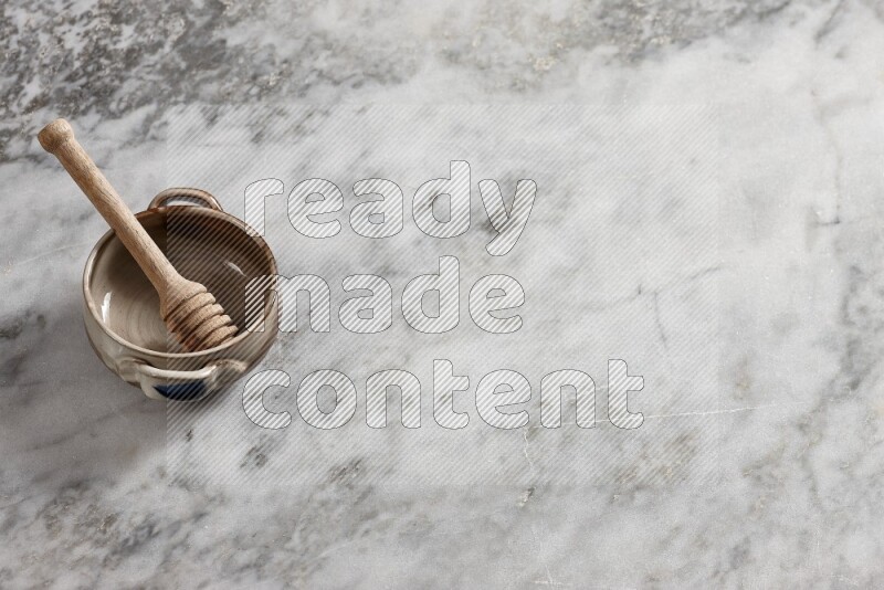 وعاء فخاري متعدد الألوان مع ملعقة عسل خشبية بداخله على خلفية من الرخام الرمادي