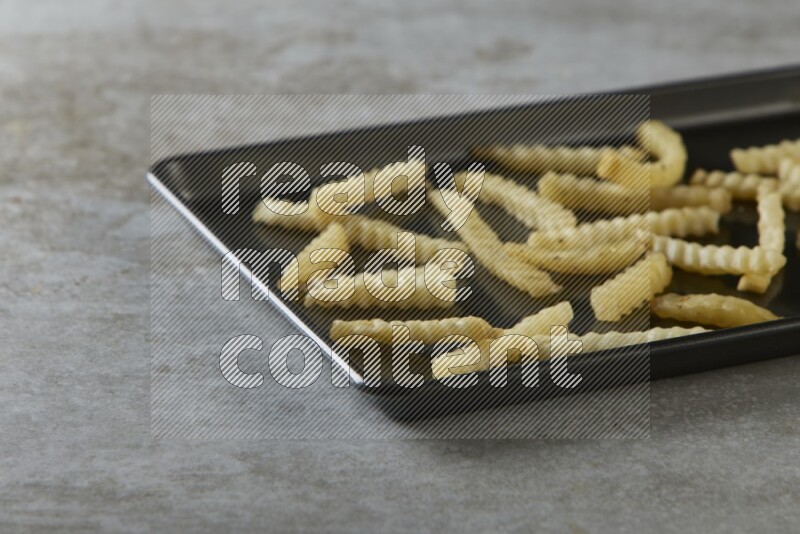 crinkle fries in a black stainless steel rectangle tray on grey textured counter top