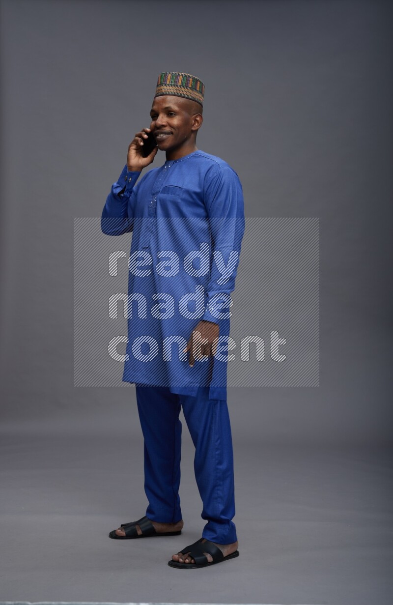 Man wearing Nigerian outfit standing talking on phone on gray background