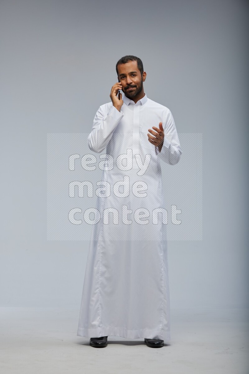 Saudi man wearing Thob standing talking on phone on Gray background