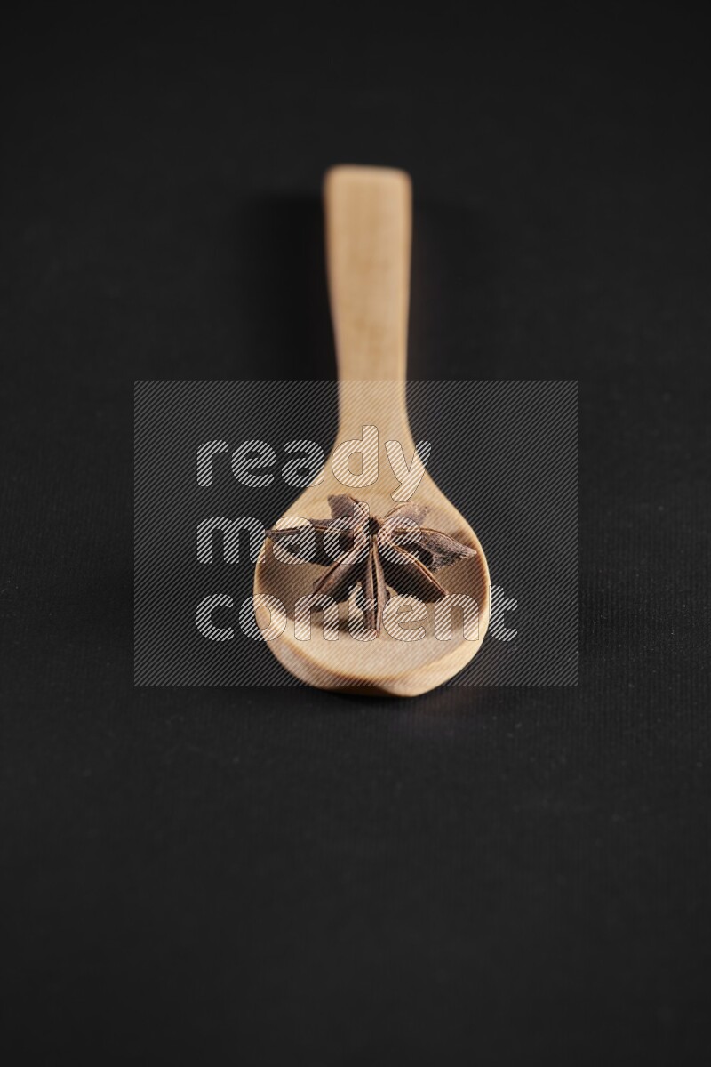 Star Anise in a wooden spoon on more stars anise filling the frame on black flooring