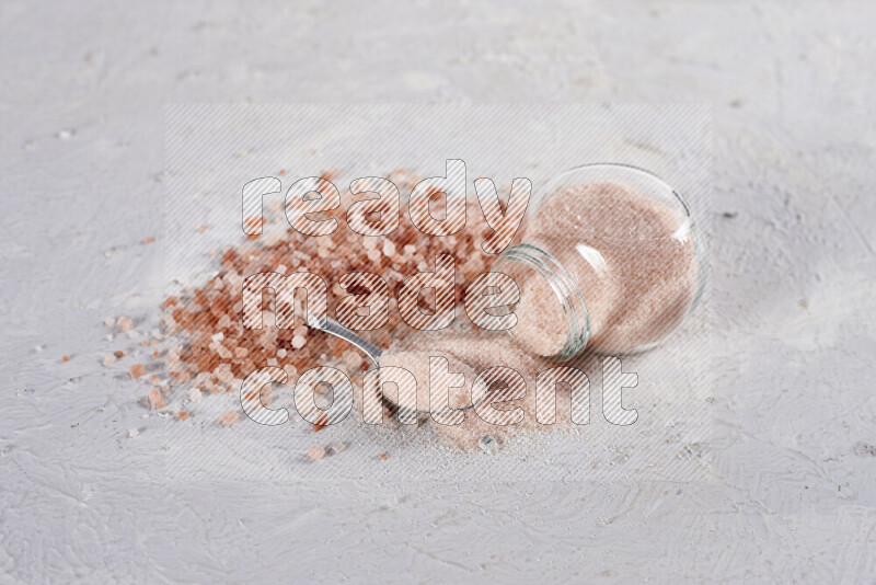 A glass jar full of fine himalayan salt with some himalayan crystals beside it on a white background