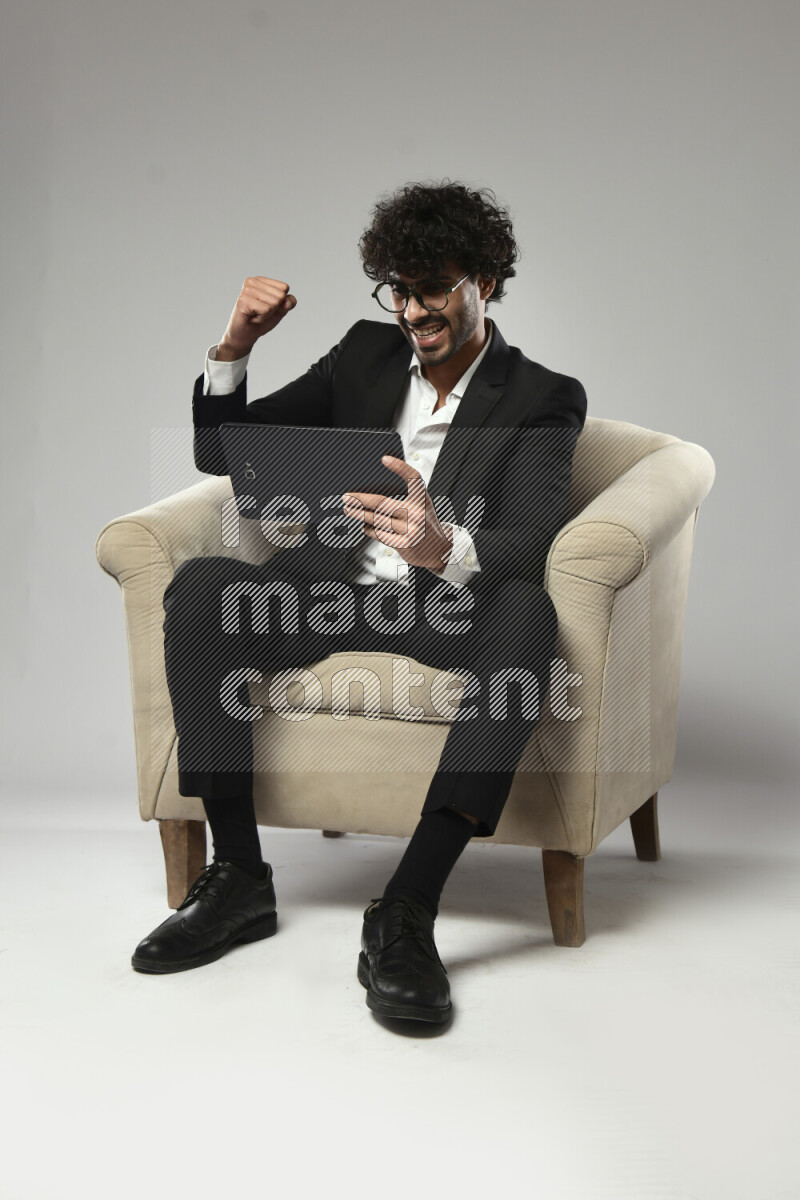 A man wearing formal sitting on a chair gaming on a tablet on white background
