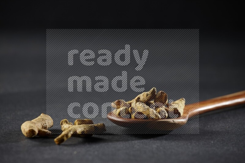 A wooden ladle full of dried turmeric fingers on black flooring