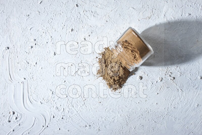A flipped glass jar full of allspice powder and powder spilled out of it on a textured white flooring