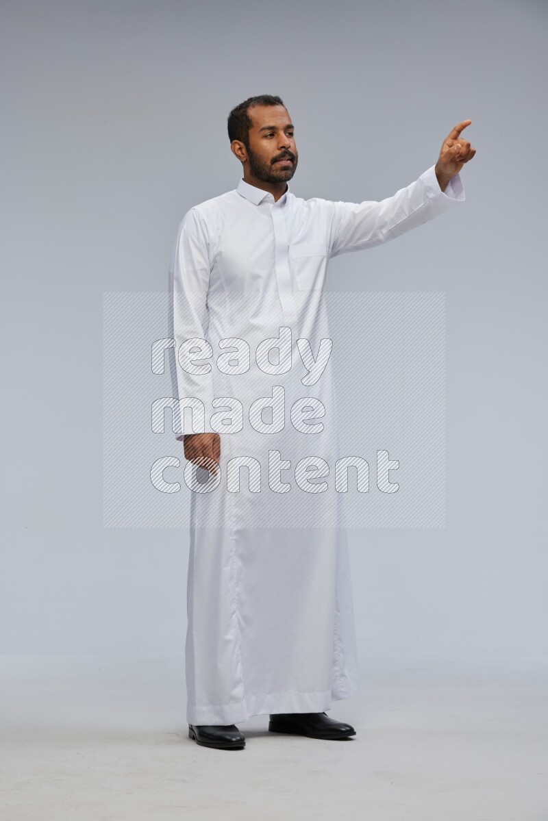 Saudi man Wearing Thob standing interacting with the camera on Gray background