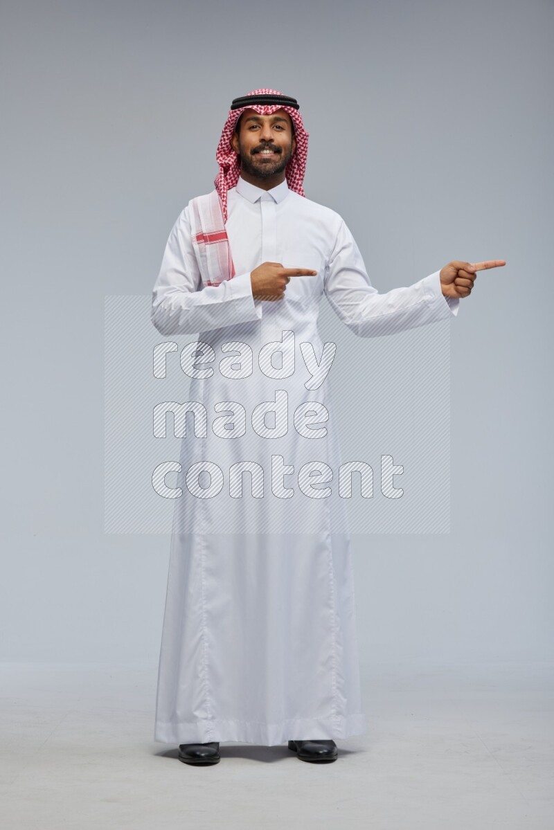 Saudi man Wearing Thob and shomag standing interacting with the camera on Gray background