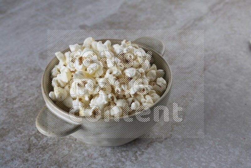 popcorn in a off-white handheld ceramic bowl on a grey textured countertop