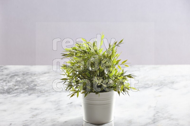 Green artificial plant in white pot on light grey marble background