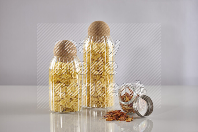 Raw pasta in glass jars with chilis on light grey background