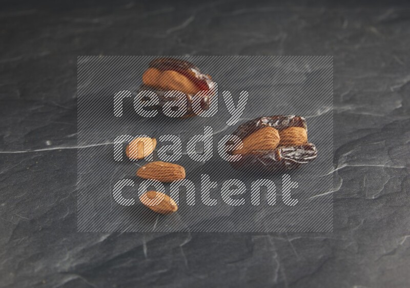 two almond stuffed madjoul dates on a black textured background
