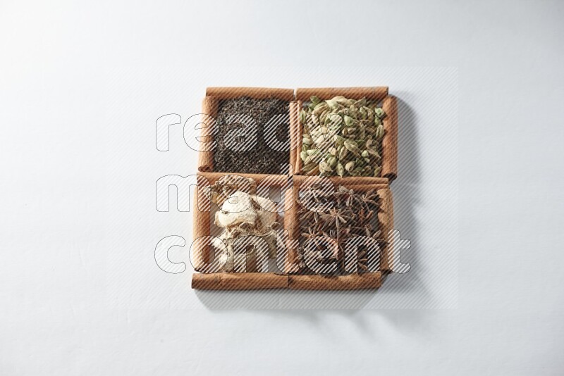 4 مربعات من أعواد القرفة ممتلئة بالشاي والهيل واليانسون والزنجبيل على أرضية بيضاء