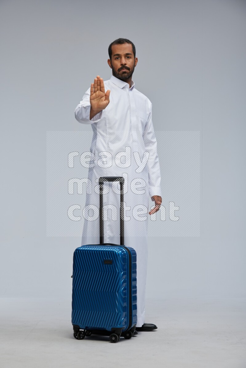 Saudi man wearing thob standing holding Travel bag on Gray background