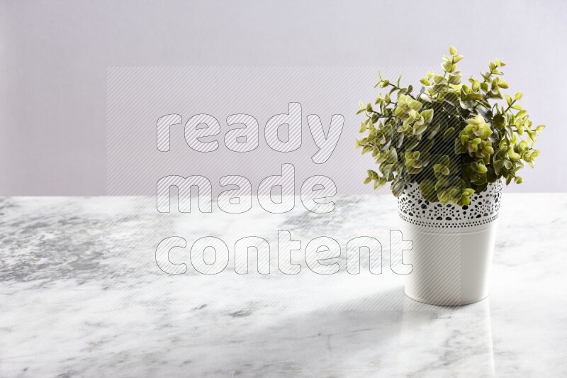 Green artificial plant in white decorative pot on grey marble background