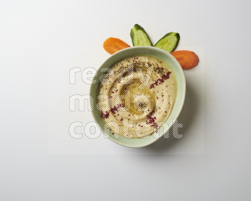 Hummus in a green plate garnished with zattar & sumak on a white background