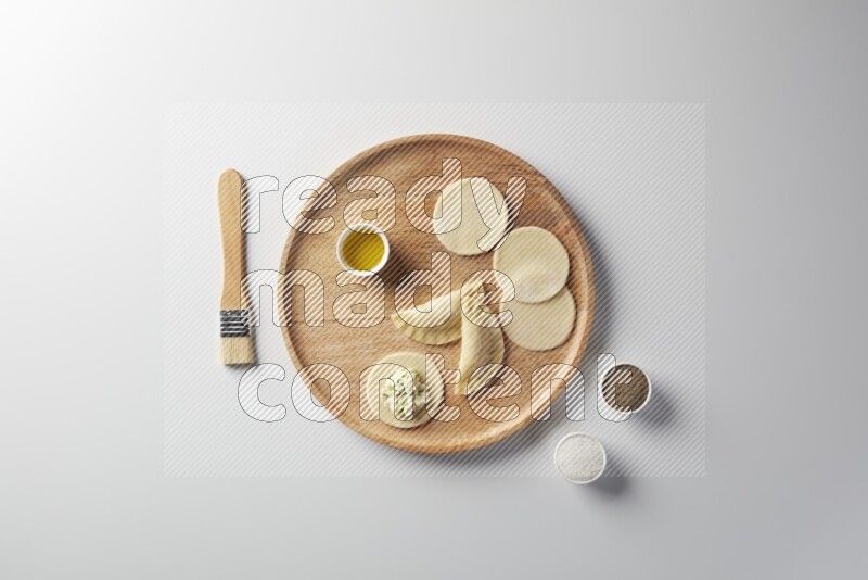 two closed sambosas and one open sambosa filled with cheese while salt, black pepper and oil with oil brush aside in a wooden dish on a white background