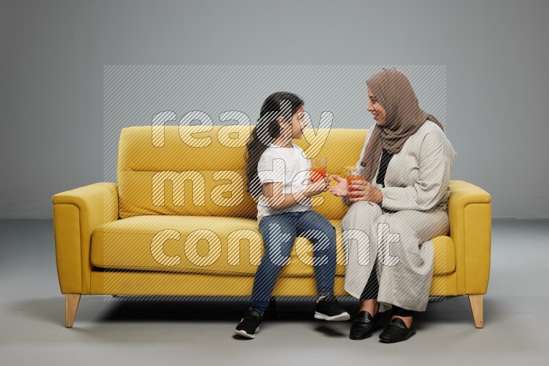 Mom and daughter sitting drinking juice on gray background