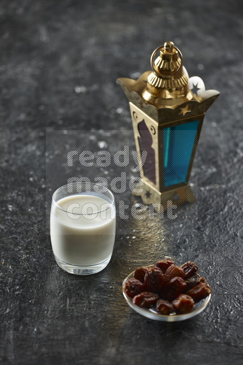 A golden lantern with different drinks, dates, nuts, prayer beads and quran on textured black background