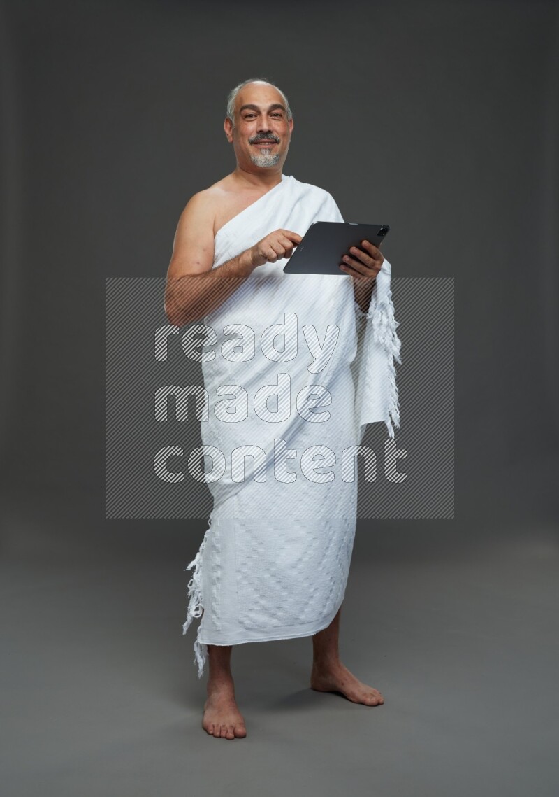 A man wearing Ehram Standing working on tablet on gray background