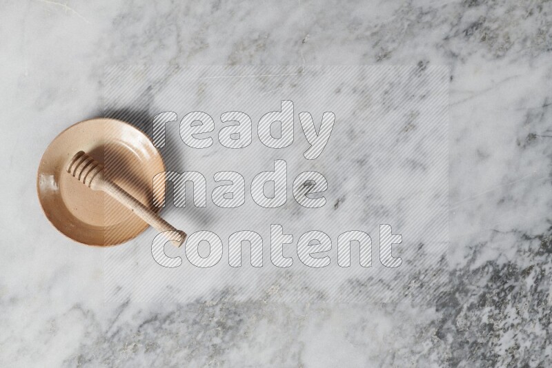 Beige pottery plate with wooden honey dipper in it on grey marble background