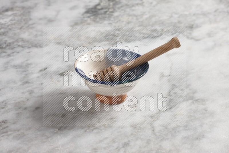 Multicolored pottery bowl with wooden honey dipper in it on grey marble background