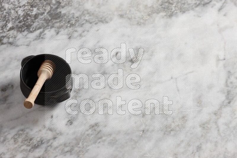 وعاء فخاري أسود مع ملعقة عسل خشبية بداخله على خلفية من الرخام الرمادي