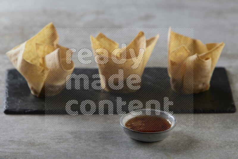 wonton cups with soy sauce ramkin on rectangle slate on grey textured counter top