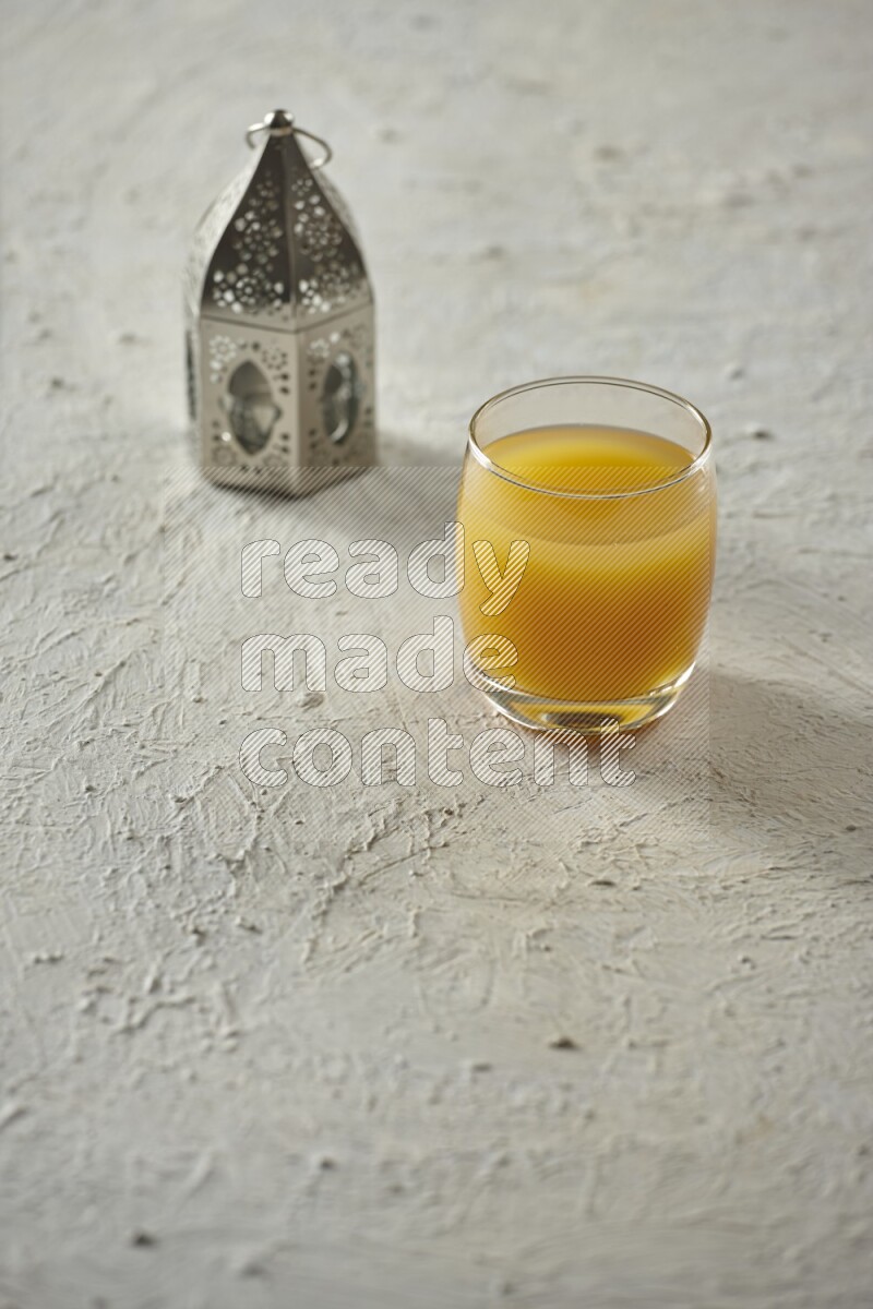 A silver lantern with different drinks, dates, nuts, prayer beads and quran on textured white background