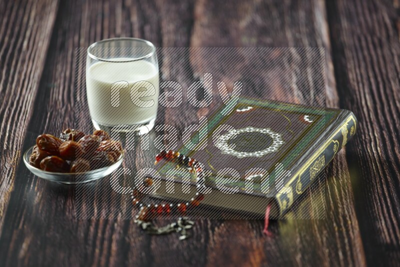 Quran with dates, prayer beads and different drinks all placed on wooden background
