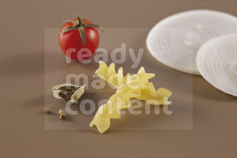 Raw pasta with different ingredients such as cherry tomatoes, garlic, onions, red chilis, black pepper, white pepper, bay laurel leaves, rosemary and cardamom on beige background