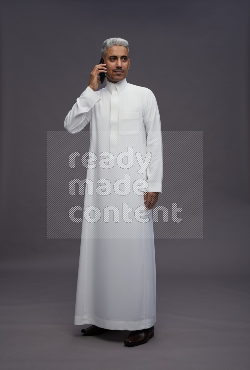 Saudi man wearing thob standing talking on phone on gray background