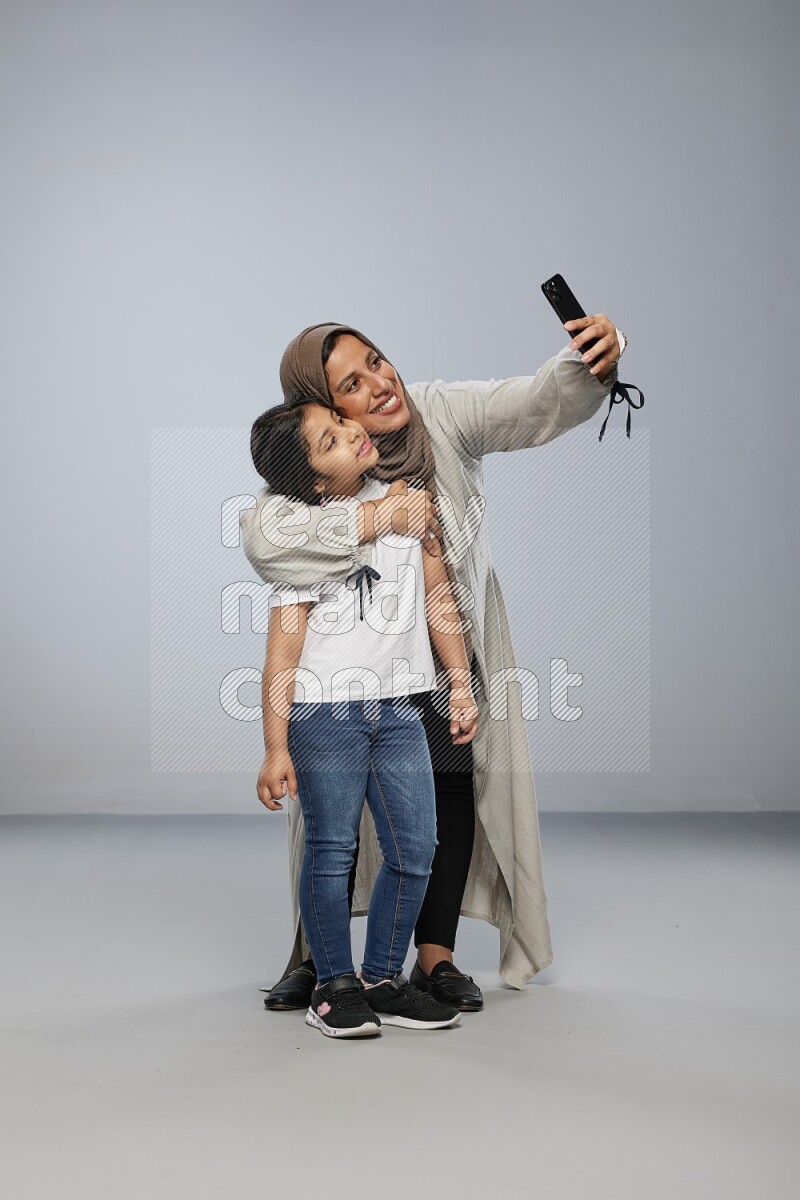 A girl standing taking selfie with her mother on gray background