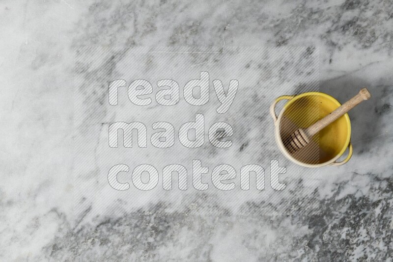 Multicolored pottery bowl with wooden honey dipper in it on grey marble background