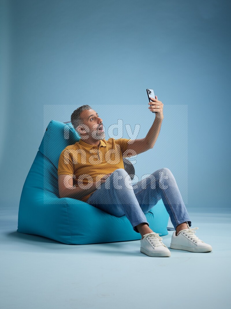 A man sitting on a blue beanbag and taking selfie