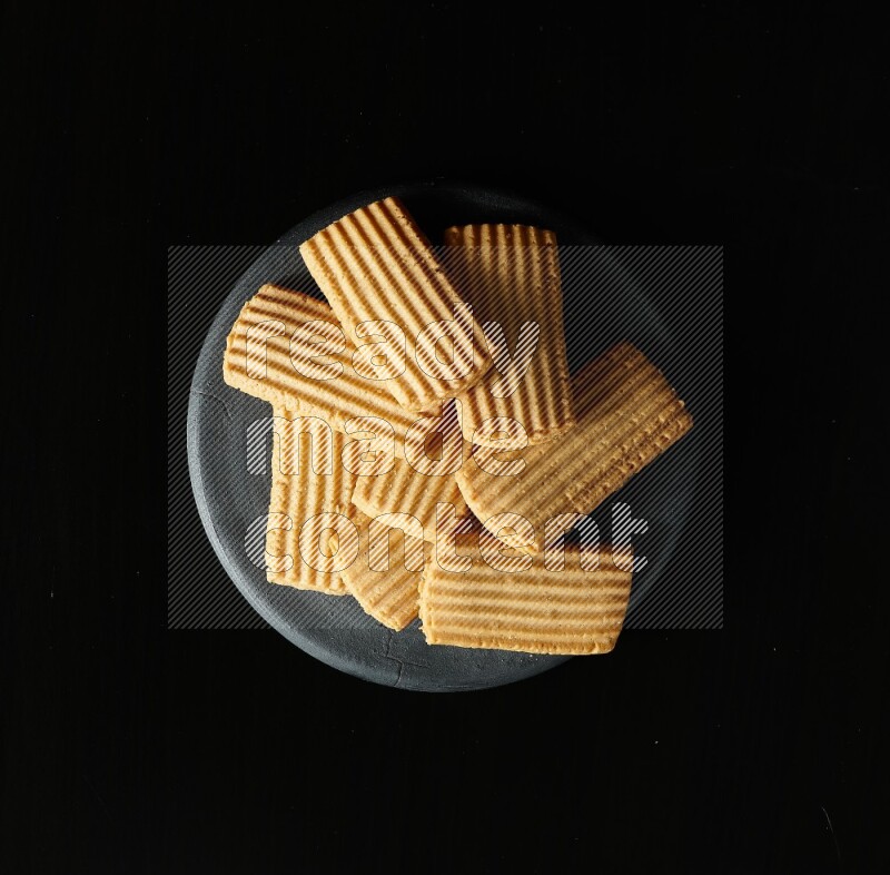 Golden biscuits in a black pottery plate on black background